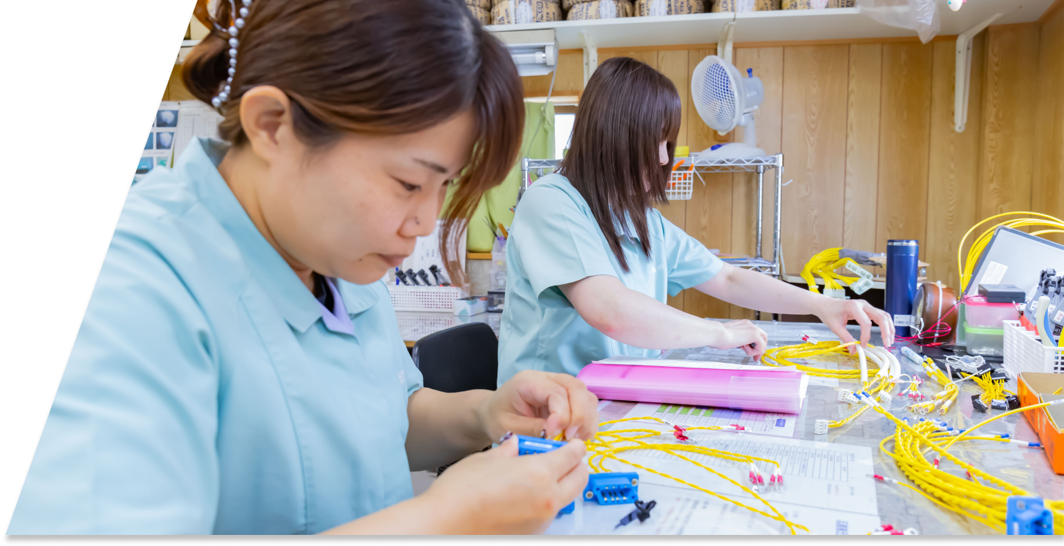 電線をカッターで加工している作業者の手元。黄色い電線と作業台の上に置かれた資料が写っている。